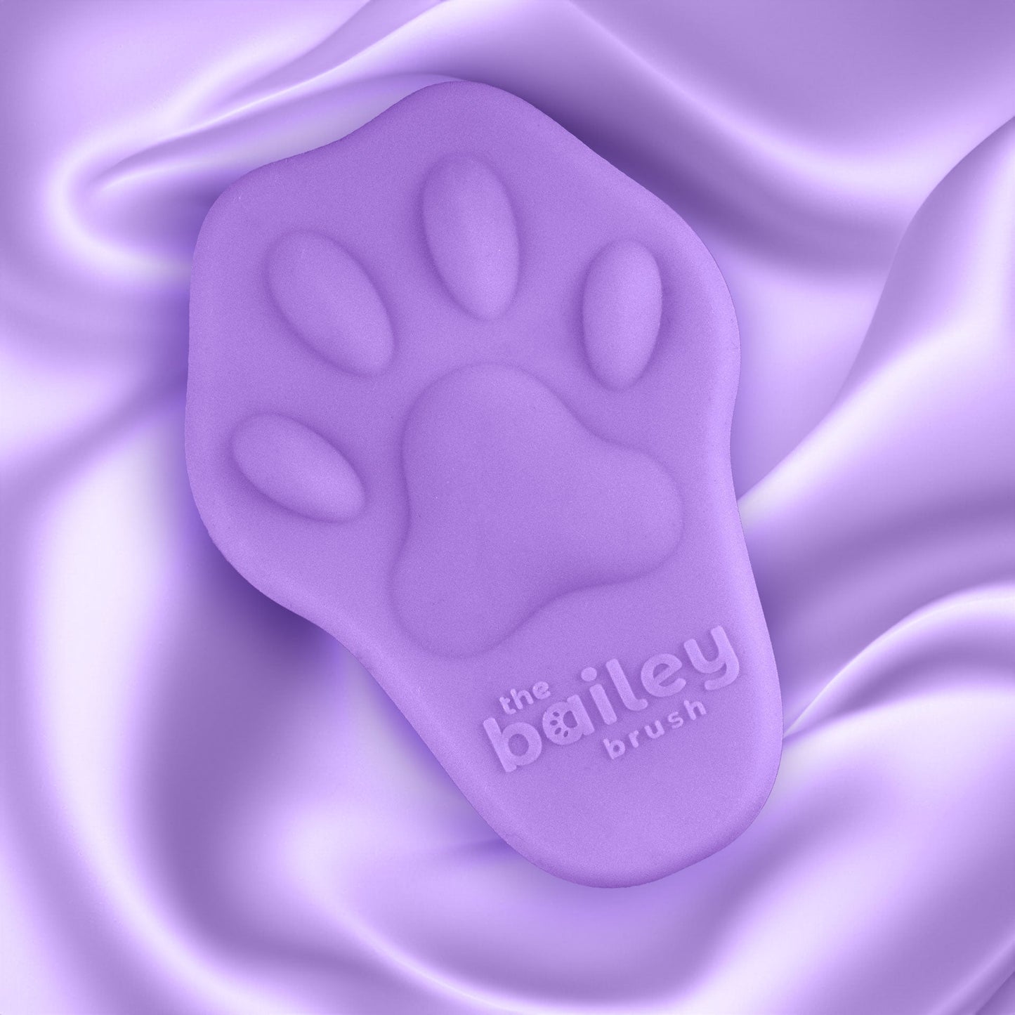Purple paw-shaped brush with 'the bailey brush' branding on a purple fabric background
