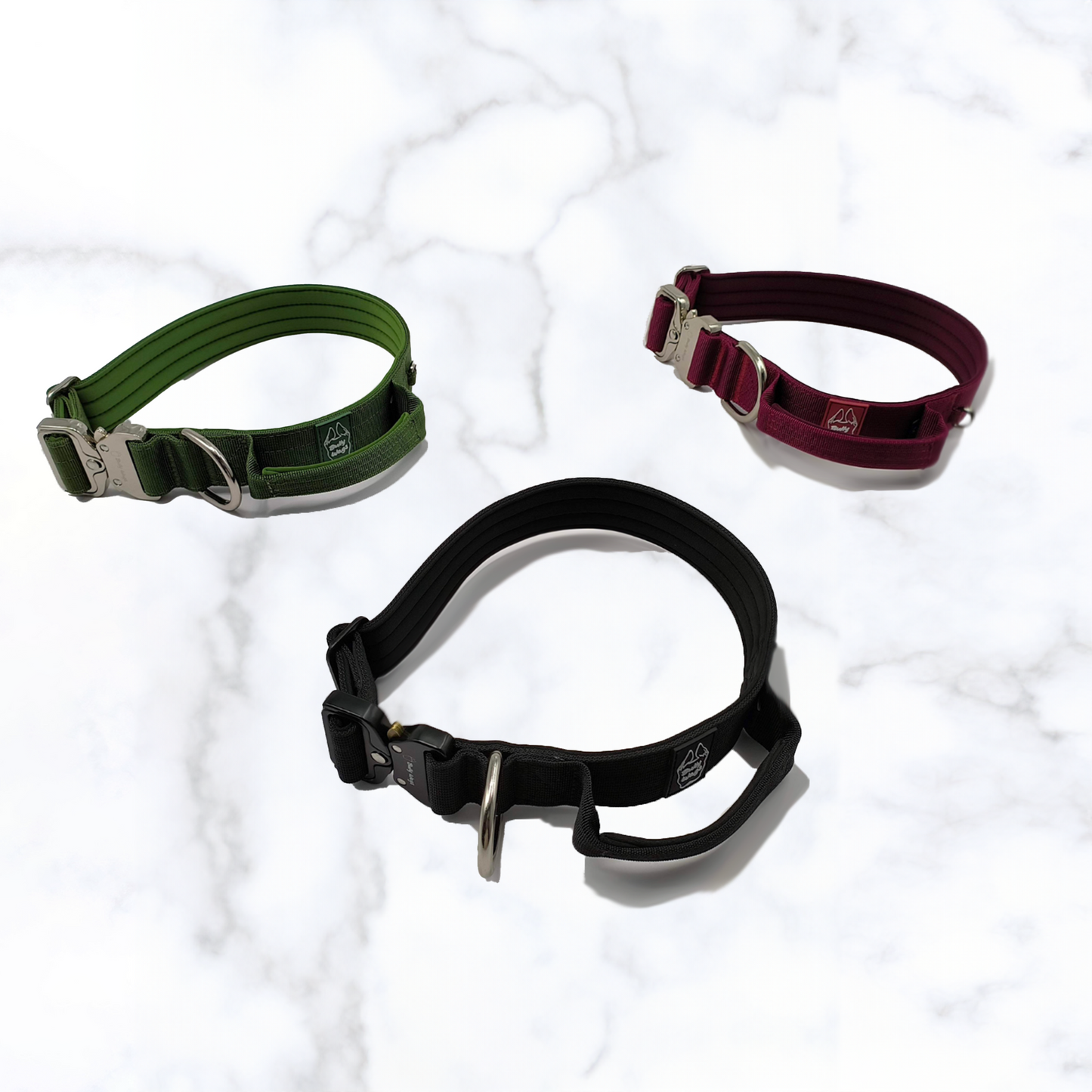 Three tactical dog collars with handles, displayed in black, green, and red colors, placed on a marble surface.