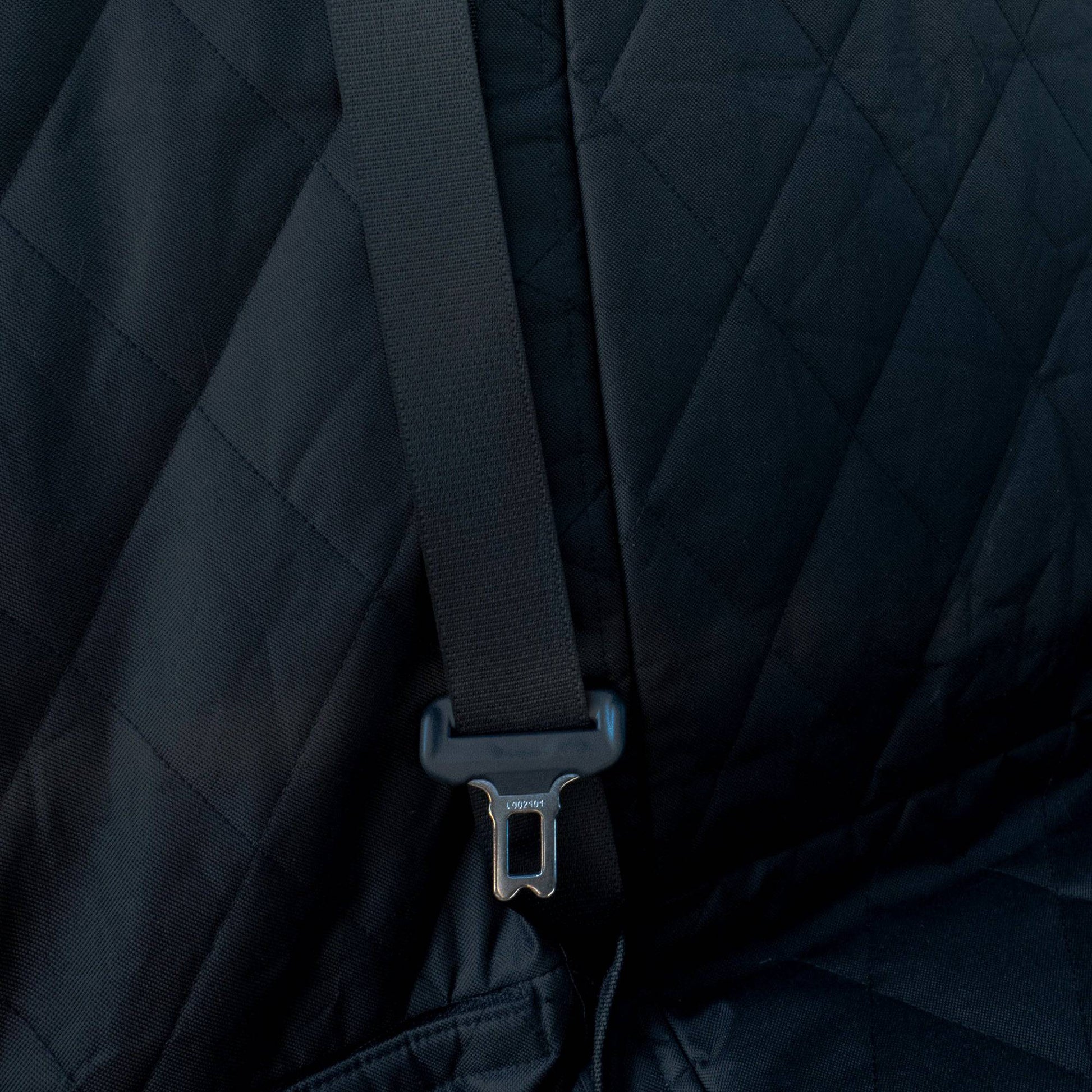 Close-up of a black quilted jacket with a strap and buckle detail.