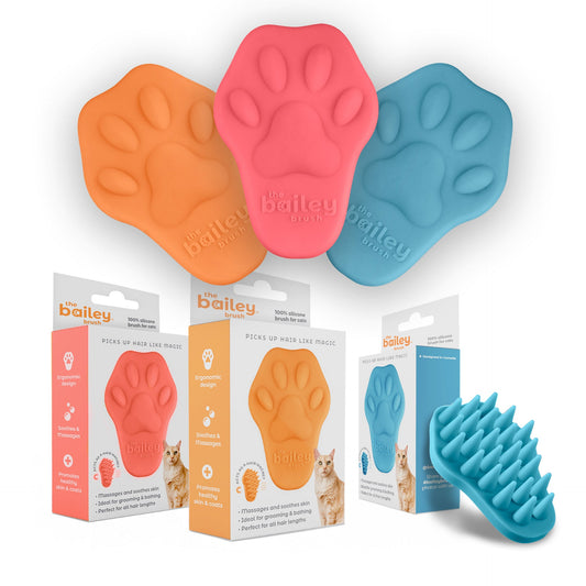 Three paw-shaped pet grooming tools in orange, pink, and blue with packaging and a brush on a white background.