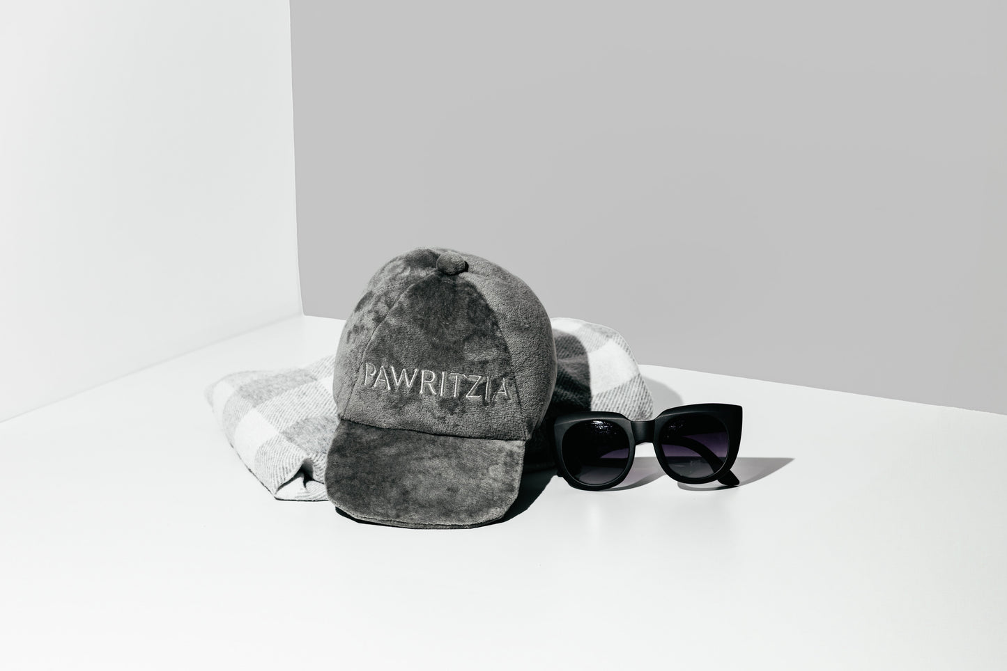 Gray cap with 'Wawrzyniec' branding and black sunglasses on a white surface.