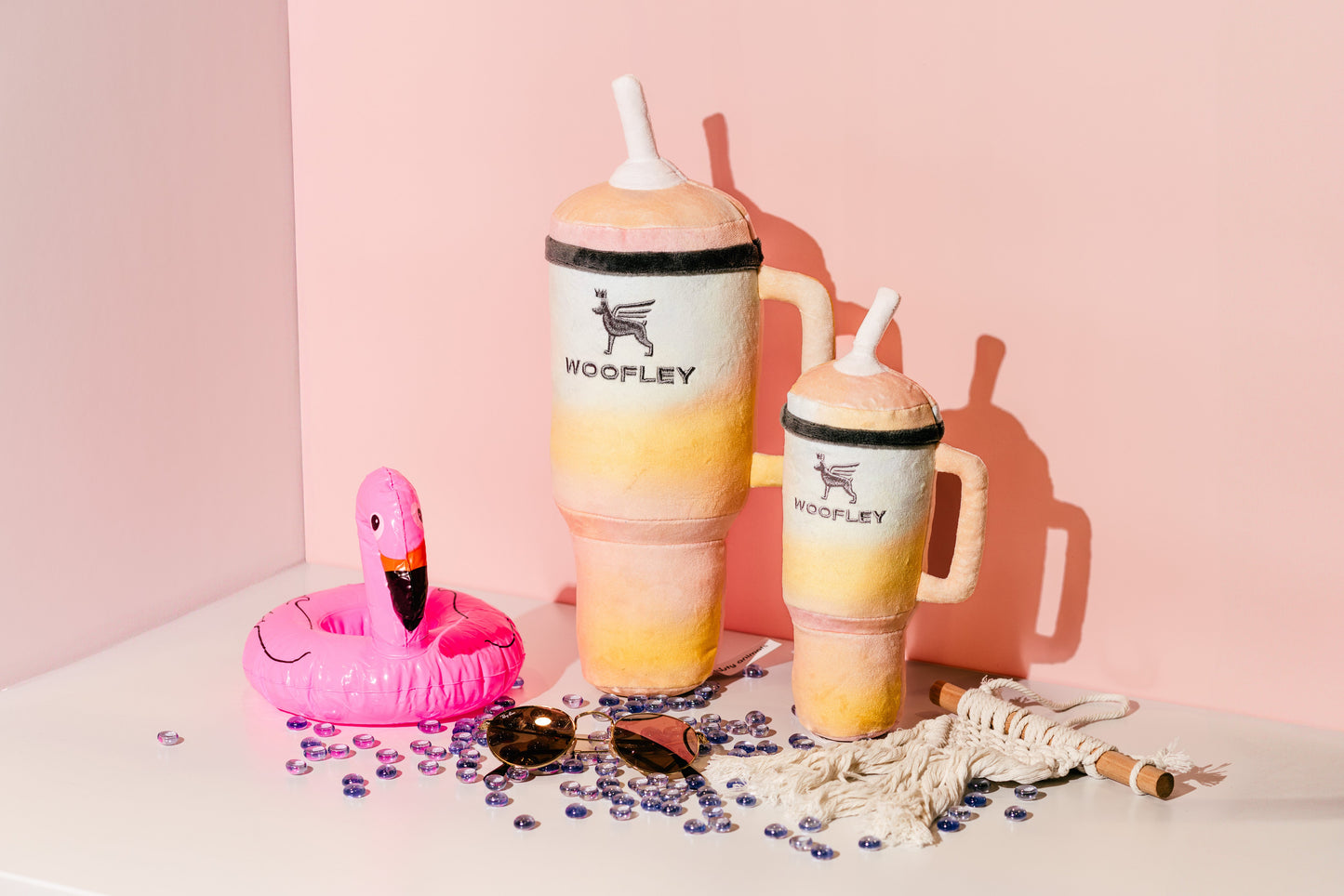 Colorful tumbler with straw, pink flamingo float, and sunglasses on a light surface with pink background