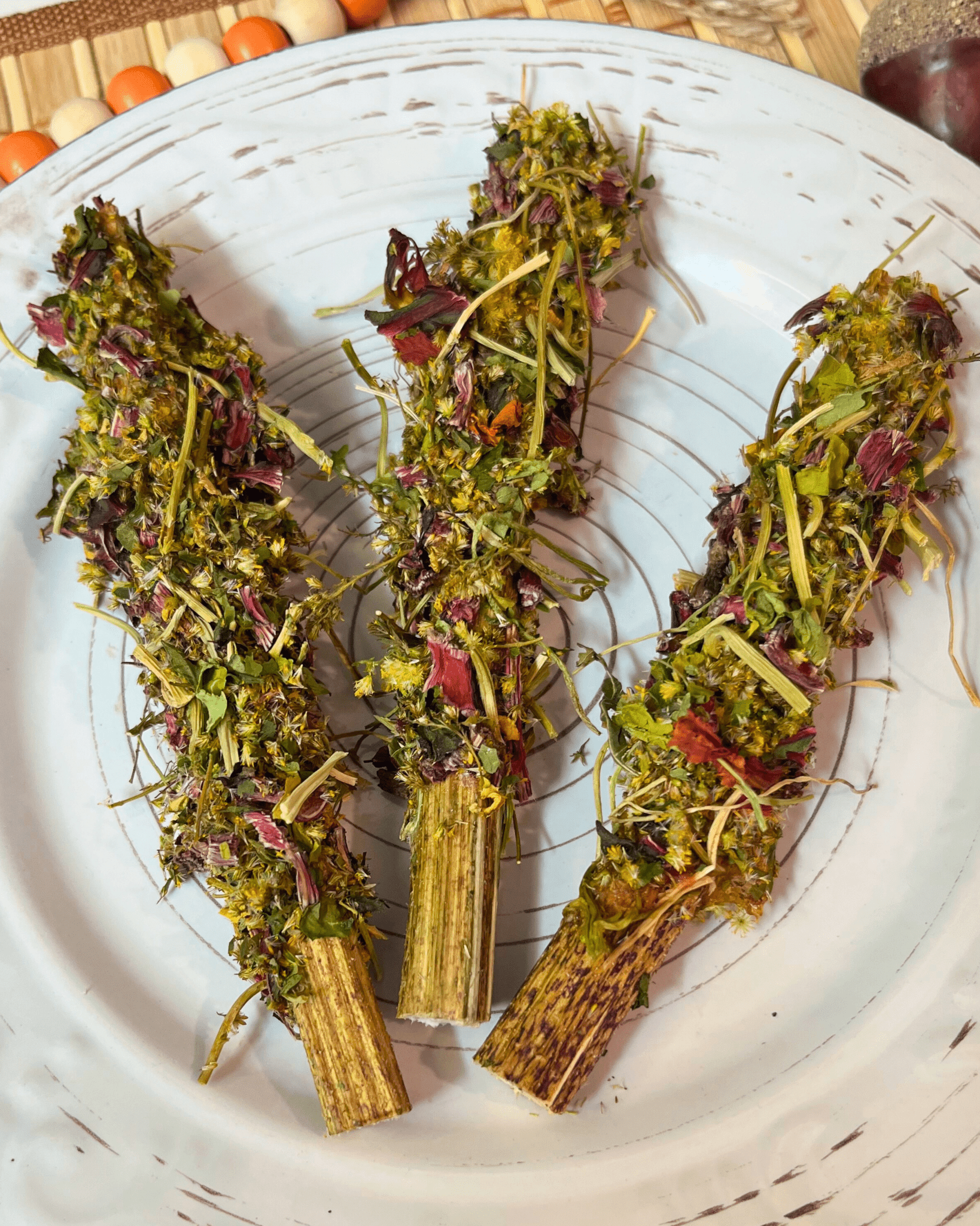 Three dried herb bundles on a white plate with a wooden surface in the background