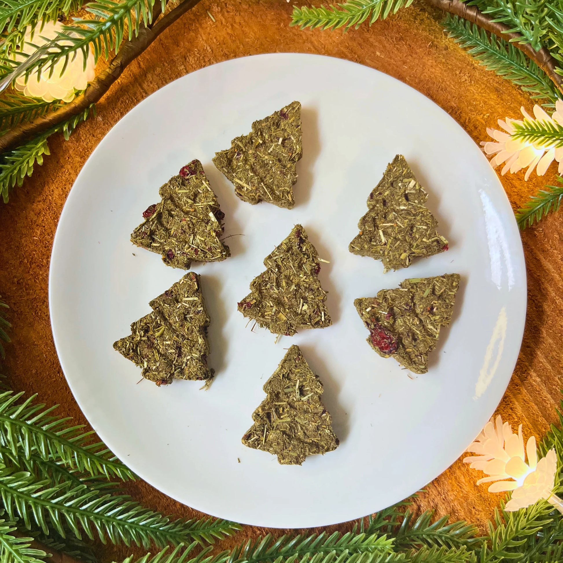 Green triangular timothy hay cookies on a white plate with Christmas tree decorations