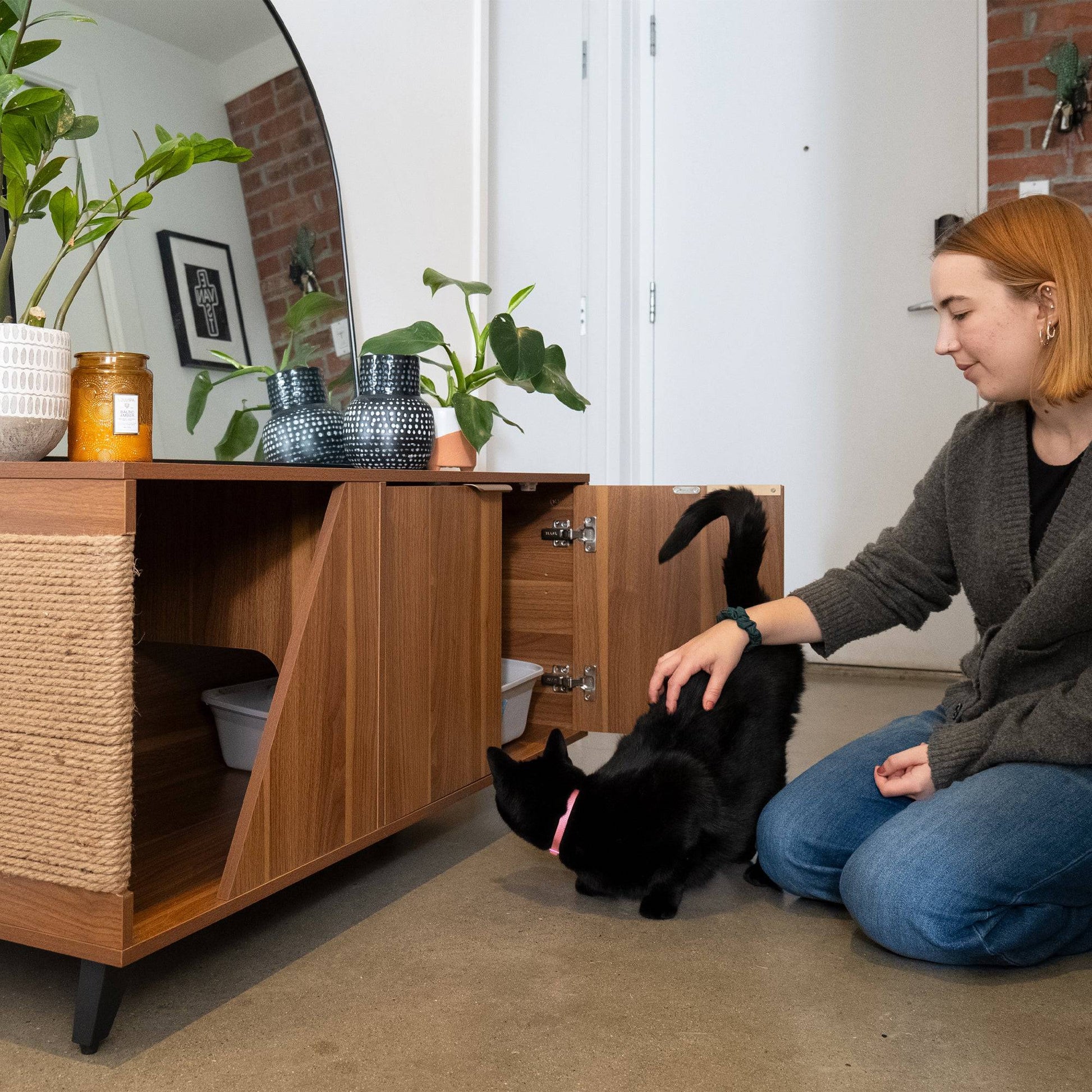 Woman petting a black cat in a room with wooden furniture and plants.