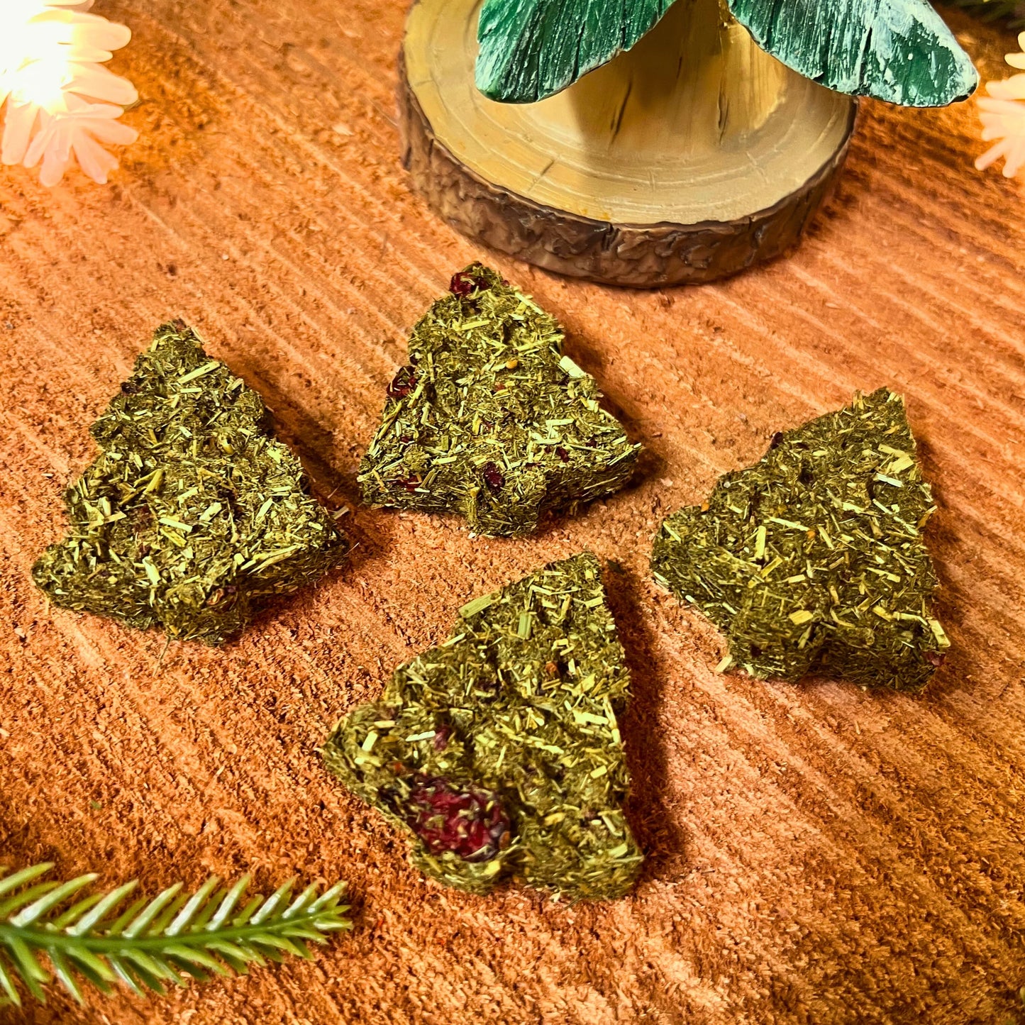 Green tree-shaped guinea pig treats on a textured surface with a decorative tree in the background.