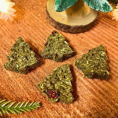 Green tree-shaped guinea pig treats on a textured surface with a decorative tree in the background.