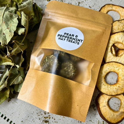 Kraft paper package of pear and peppermint hay treats with a label, surrounded by hay and dried apples.