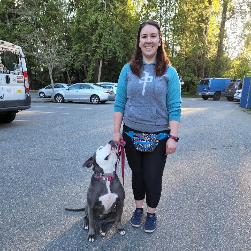 Woman standing with a dog on a leash in a parking lot with trees in the background