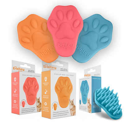 Three paw-shaped pet grooming tools in orange, pink, and blue with packaging and a brush on a white background.