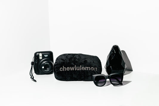 Black camera, sunglasses, and pouch with 'chewlulemon' branding on a white background