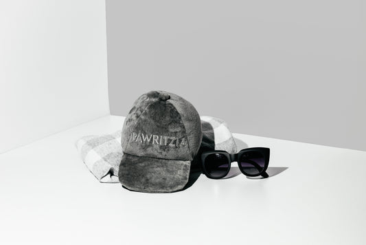 Gray cap with 'Wawrzyniec' branding and black sunglasses on a white surface.